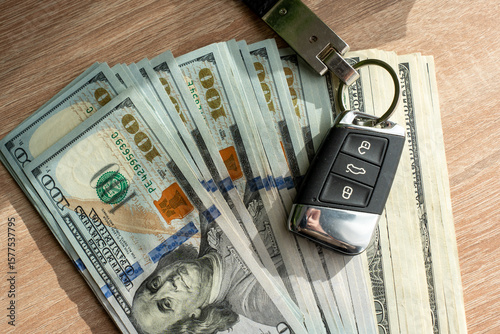 Close-up of US hundred dollar banknotes and modern car remote key on wooden surface in natural light. Symbol of financial planning, cash savings, luxury purchase, and automotive investment.