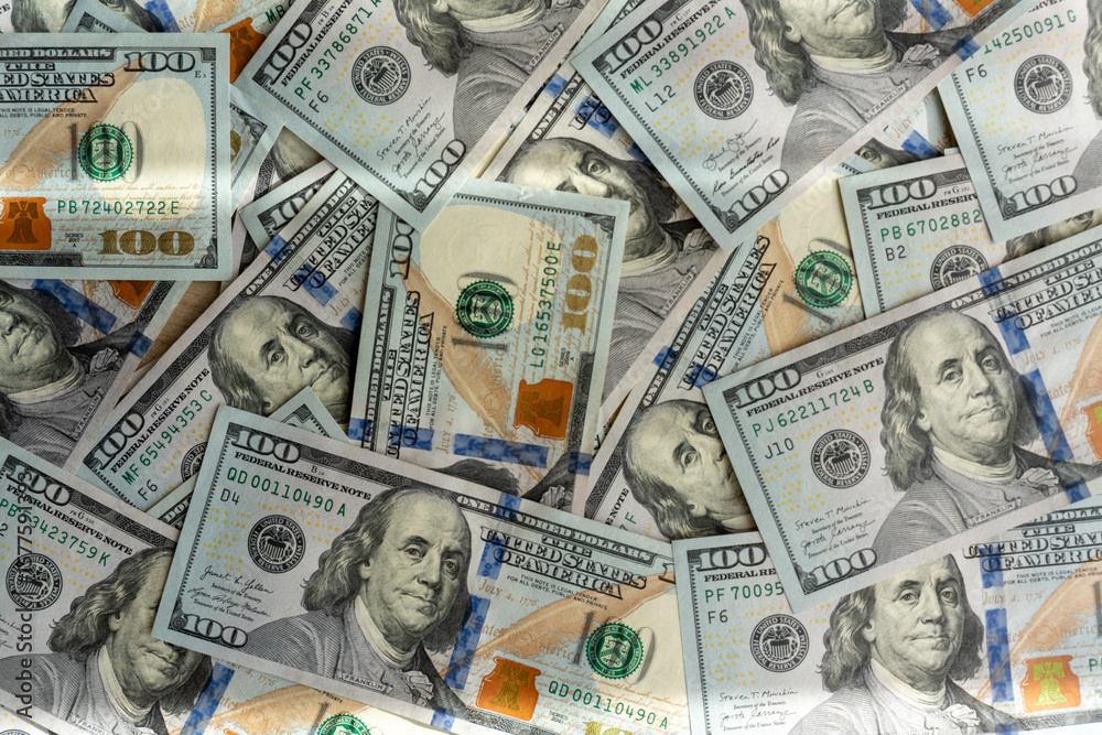 Fototapeta premium Pile of scattered US hundred dollar bills on wooden table in daylight. Concept of cash money, financial wealth, economic savings, investment and business profit.