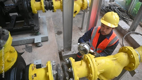 Engineer is checking pressure gauges on large gas pipelines inside a plant checking 