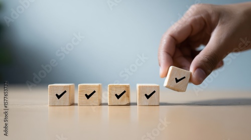 Wooden blocks with checkmark icons are arranged on table, symbolizing achievement and progress. hand is placing block, emphasizing importance of completing tasks and goals
