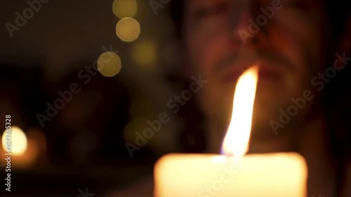 Man meditates peacefully by candlelight in a dimly lit room with soft bokeh.