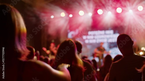 Woman raises hand at outdoor concert or worship event, with colorful stage lighting and blurred background. Ideal for music, celebration, church or festival atmosphere footage. 4K backside medium shot