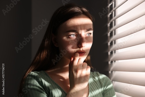 Fotografia Paranoia. Worried woman near window at home