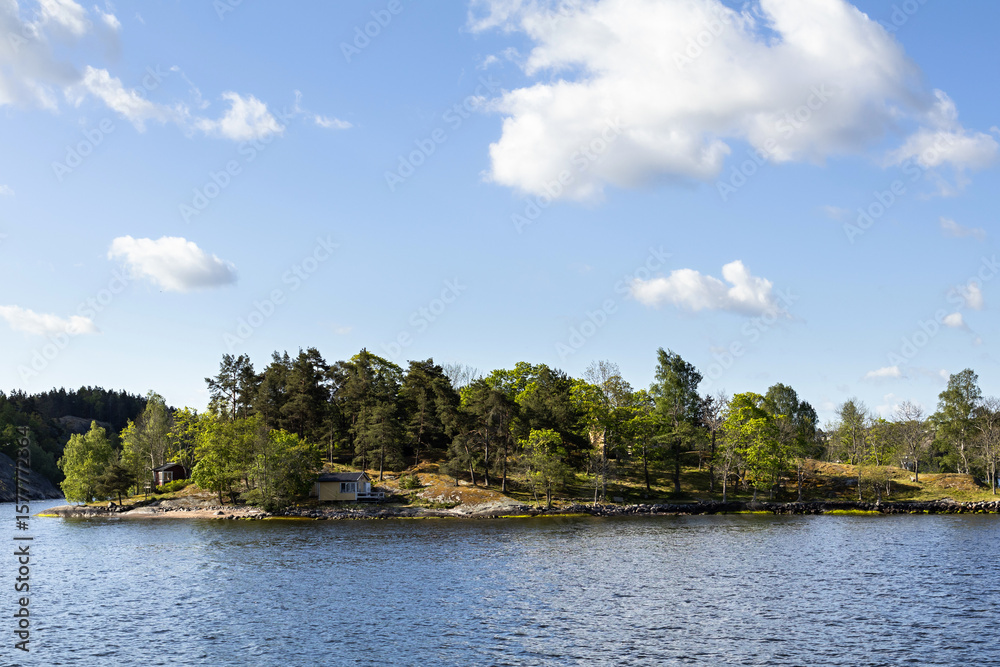 Obraz premium Stockholm archipelago green trees forest island in Baltic sea. Sunny spring summer day boat view with blue sky in Sweden. Typical scandinavian and Nordic nature landscape scenery.