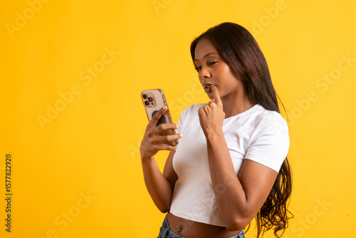 Pensive model using smartphone on vibrant yellow background