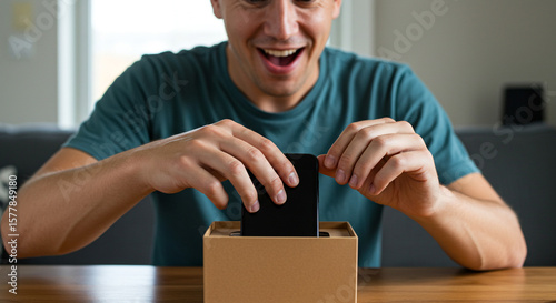Wallpaper Mural Man excitedly unboxing a new smartphone sitting at a wooden table with a green shirt on indoors Torontodigital.ca
