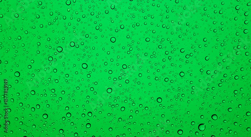 A vivid green background covered in numerous water droplets of varying sizes and circular shapes
