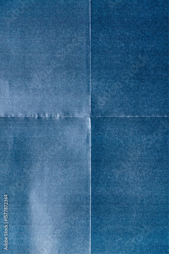 macro photo of blue paper with prominent fold marks forming a cross pattern. The texture is slightly fibrous with visible creases, giving the surface a worn, authentic poster-like look.