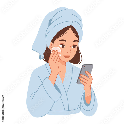 Woman in bathrobe and towel using cotton pad on face while looking at smartphone in her hand indoors