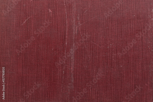 Close-up of worn antique red book cover with heavy texture and signs of age
