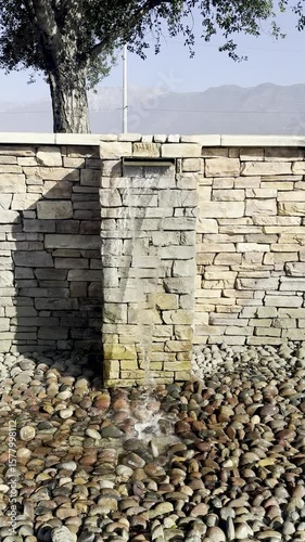 gentle water cascades over a textured stone garden wall surrounded by lush greenery creating a soothing tranquil ambiance perfect for relaxation meditation and outdoor serenity