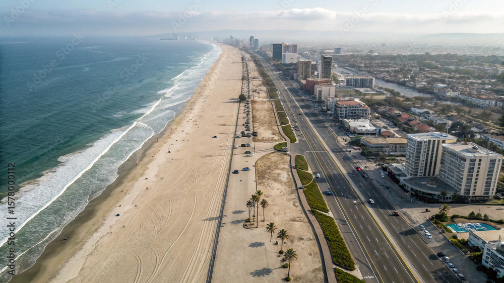 Fototapeta premium Aerial view of a beach with waves crashing on the shore next to a city with tall buildings and a road created with generated ai