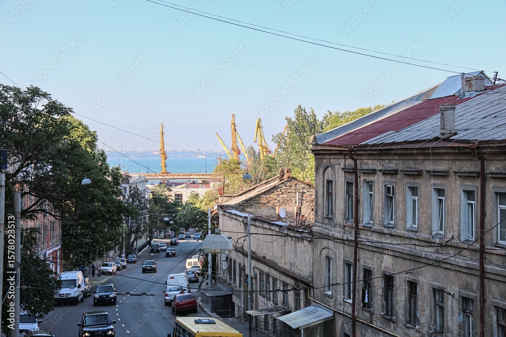 Obraz premium Old residential buildings with wires and street view leading to port cranes and sea