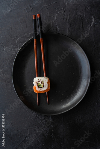 Overhead view of a Salmon California roll on a pair of chopsticks on a plate