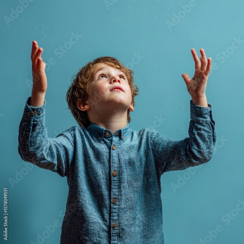 boy holding both hands up as if catching rain expressive pose light blue background
