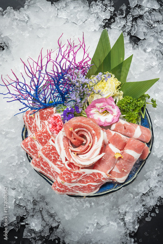 A fresh hotpot meat platter featuring thinly sliced Japanese beef and Kurobuta pork belly, photographed from a bird’s eye view against a backdrop of crushed ice.
