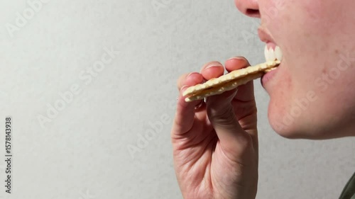 Side view of a woman taking a bit of a sandwich made with two saltine crackers captured against a neutral gray background