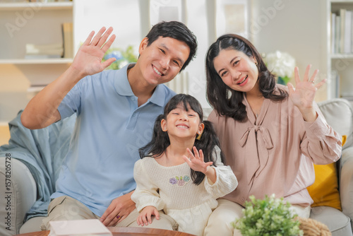 Portrait of happy multi-generation Asian family with dad mom and kids using smartphone digital tablet for video call while sitting on sofa at home during family bonding relaxation time