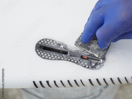 Surfboard repair process showing a worker fixing a fin box with a sanding tool.