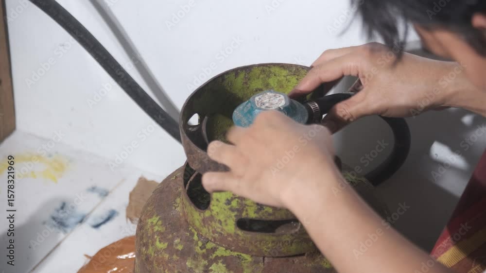 A man installs a gas regulator onto a gas cylinder, then removes it and attempts to pry it off again using scissors. His careful yet improvised actions reflect a hands-on approach to household tasks