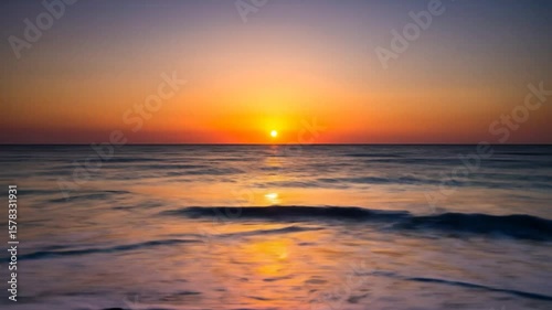 Sunrise over calm ocean waters and dark sandy beach