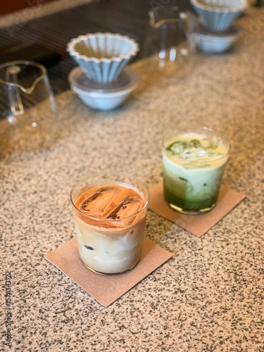 Iced matcha latte and iced coffee latte served in clear glasses on a textured countertop, perfect for a cozy café vibe and refreshing afternoon treat.