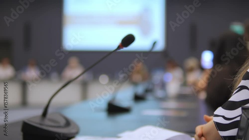 Woman sits at a table with a microphone in front of her. The microphone is black and silver