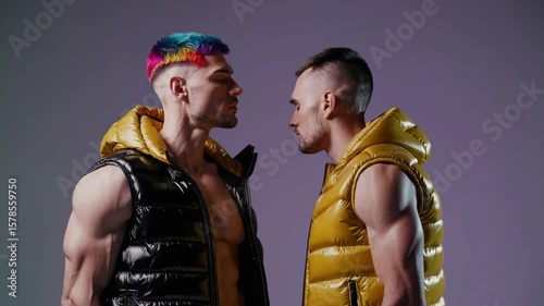 Bold queer fashion – two fit men in glossy puffer vests, rainbow hairstyle