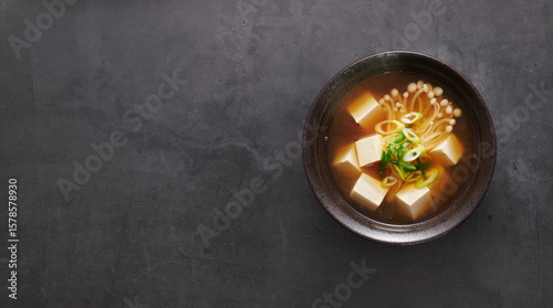 Japanese Miso Soup with Tofu and Enoki Mushrooms, on black background, top view, copy space