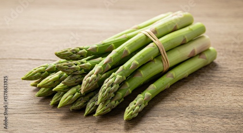 A bundle of fresh green asparagus tied with a rubber band on a textured wooden surface close up view