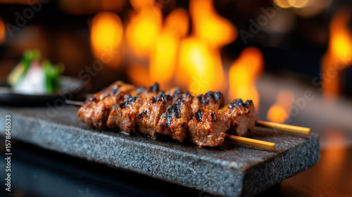 Grilled meat skewers served on a stone plate with a warm, fiery background creating a cozy dining ambiance.
