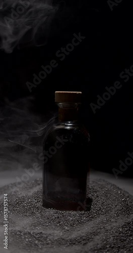 bottle filled with rich brown liquid stands prominently among swirling smoke on a dark sandy surface The scene evokes a sense of intrigue and mystery in a moody environment