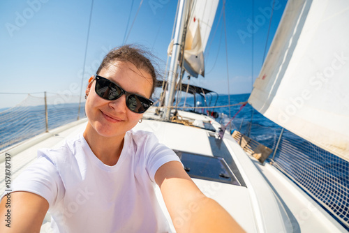 Fototapeta Happy young woman sitting on the bow of a sailing yacht with full sails near Croatia