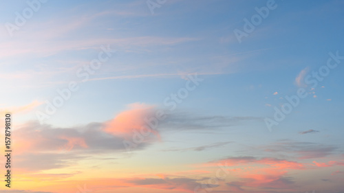 Soft pink and orange clouds drift across a calm blue morning sky as the sun begins to rise.
