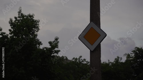 A handheld camera captures a signal stop against a backdrop of dramatic, moving clouds, creating a sense of anticipation and the passage of time.