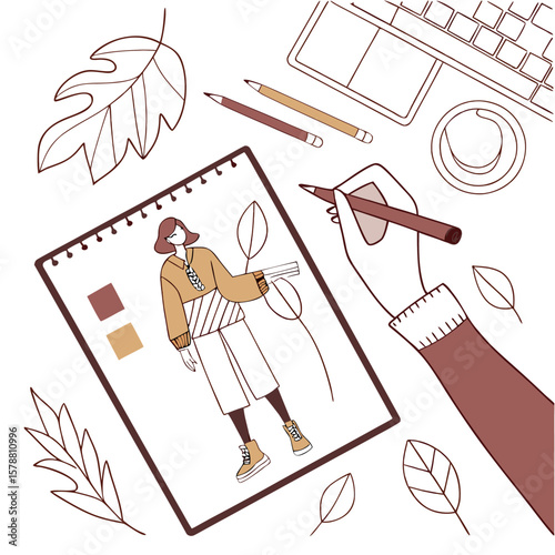 Overhead view of a person s hand sketching a fashion design of a woman in a sweater and skirt with autumn leaves and a laptop on a desk