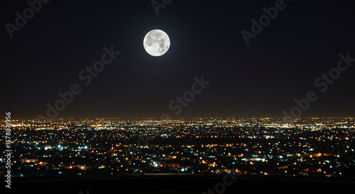 Fototapeta Naklejka Na Ścianę i Meble -  Full moon over a city at night, illuminated by city lights.