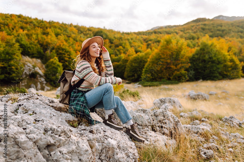 Fototapeta premium Young woman hiker with a briefcase on a mountain trail enjoying nature. Traveler on a hike and feeling freedom in the open air. Hiking, travel and nature concept. Active lifestyle.