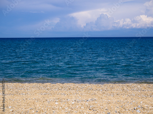 Fototapeta Naklejka Na Ścianę i Meble -  Tranquil blue sea with sandy shore under a cloudy summer sky, ideal for travel, calmness, and wellness designs.