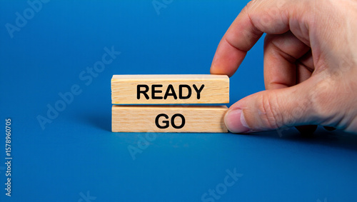 A hand is placing a wooden block with the word ready on top of another block with the word go, symbolizing readiness