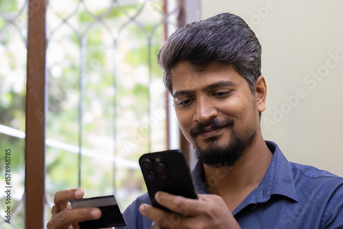 Happy Asian Indian man shopping online with smart phone and making payment using the credit card