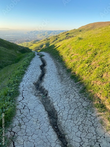 Cracked earth along hiking trail in a rolling green landscape at dusk with distant city views