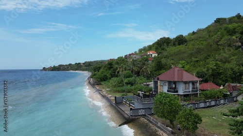 Scenic aerial view of a beach guesthouse on the coast of Nusa Penida island, surrounded by tropical vegetation and turquoise waters.