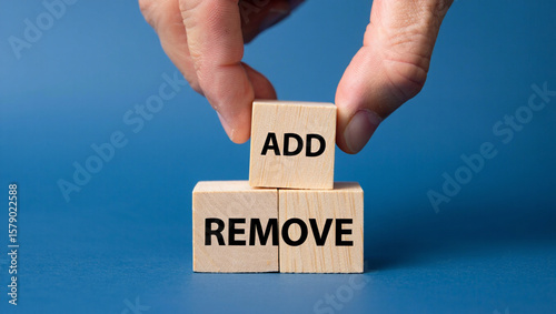 A hand places a wooden block with the word add on top of two blocks with the word remove