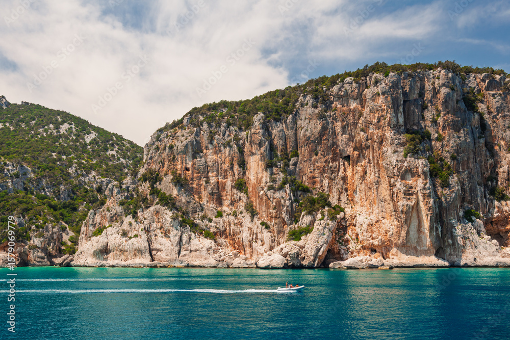 Boat traveling along vertical cliff coastline on Sardinian Orosei Gulf