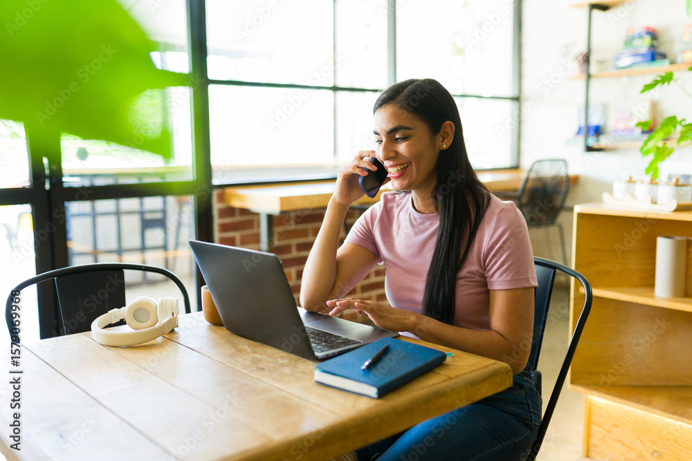 Obraz premium Freelancer working remotely in coffee shop using laptop and talking on phone