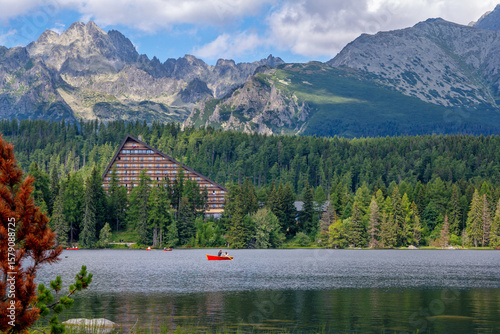 Scenic summer view of Strbské Pleso in the High Tatras, Slovakia. Tourists enjoy peaceful boat rides on the crystal-clear mountain lake, surrounded by a lush green forest