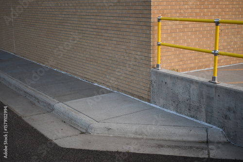 Fototapeta Naklejka Na Ścianę i Meble -  Sidewalk ending at brick building. Yellow metal railing.