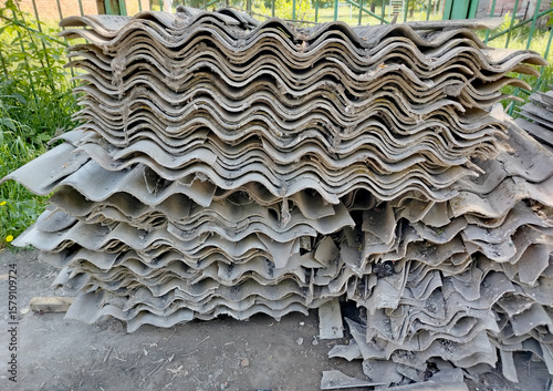 Old gray slate, stacked in uneven piles and broken into pieces of different shapes and sizes. Construction waste after roof repair