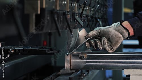 Sheet metal bending on CNC machine. Gloved worker bending a metal sheet using a CNC press brake in an industrial setting focused on precision manufacturing.